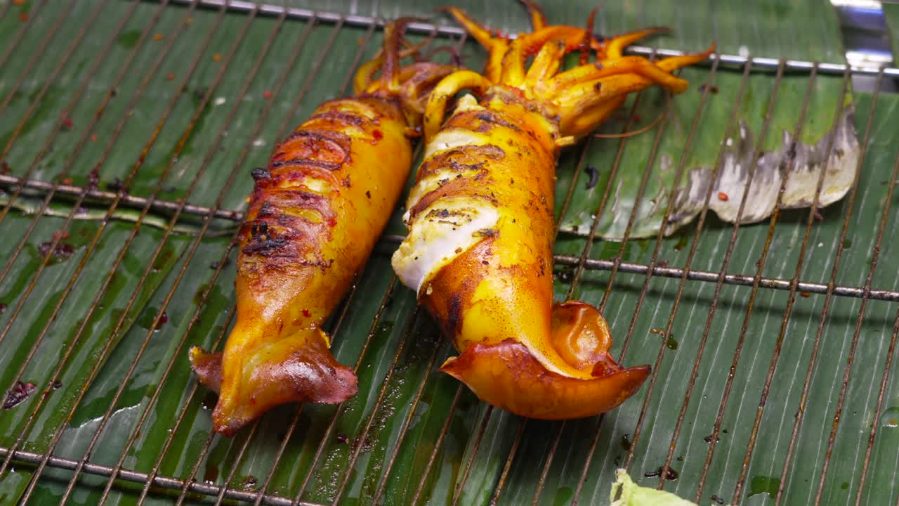 Fresh grilled stuffed squid served on banana leaf with wire rack at traditional Thai street food market, showcasing authentic seafood preparation and local culinary culture