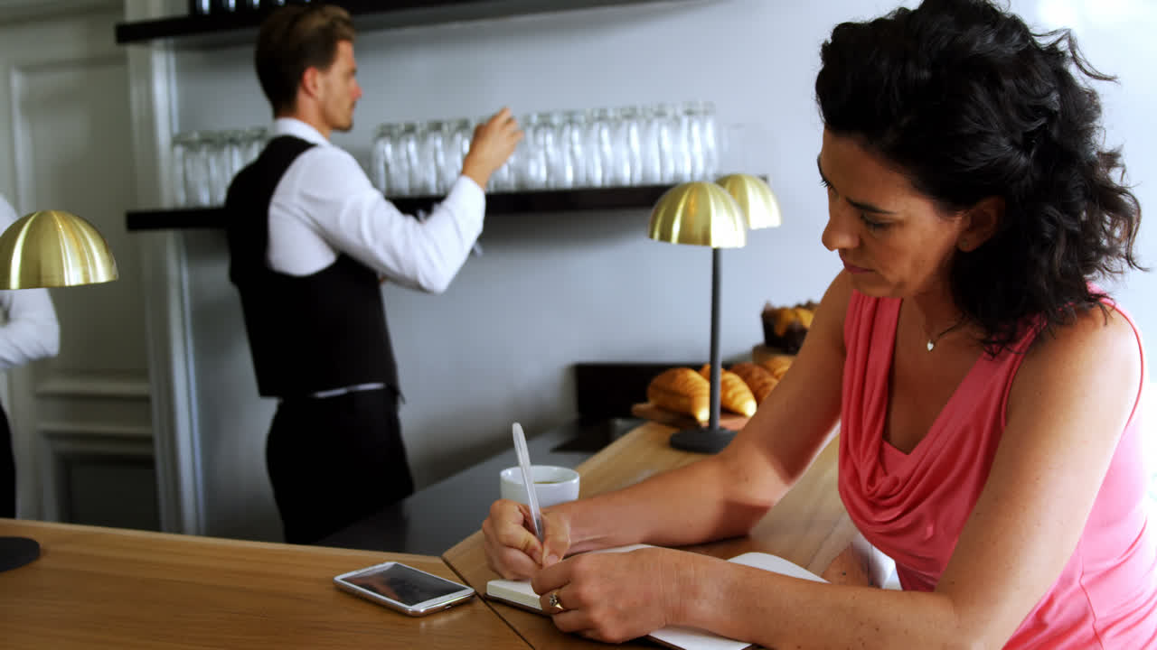mujer escribiendo en un diario en el mostrador de la barra