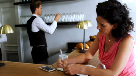 woman writing on a diary at bar counter