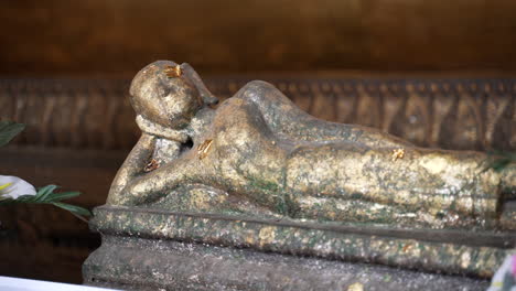 Panning-close-up-clip-of-reclined-statue-of-Buddha,-with-offerings-of-flowers-and-gold-leaf