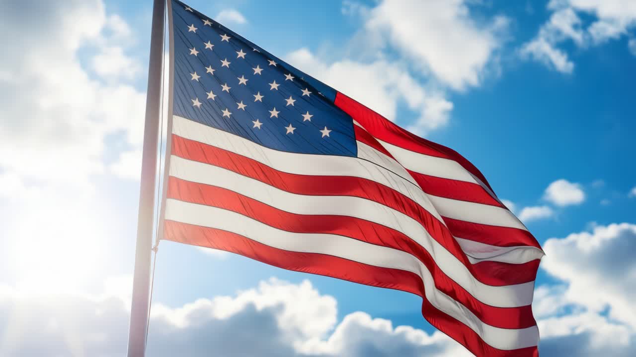 Ripresa video dal basso che mostra la bandiera americana che sventola su un cielo luminoso e nuvoloso, catturando un senso di...
