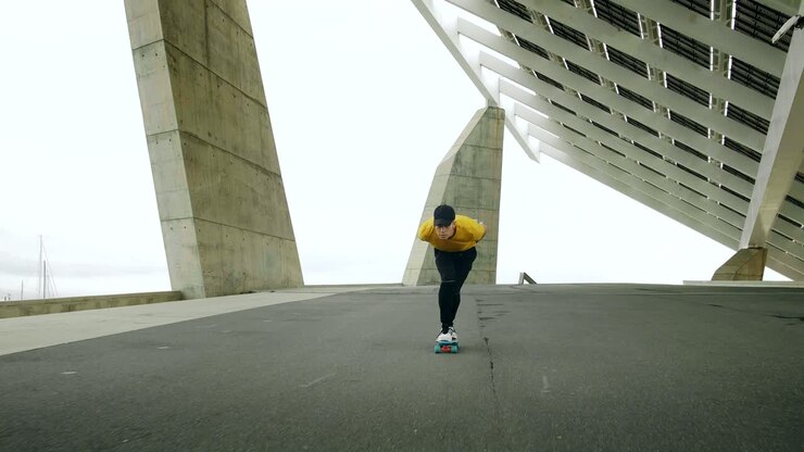 Ritratto epico e primo piano di un giovane uomo attraente e alla moda che fa skateboard velocemente sotto un pannello solare in una mattinata di sole con uno sfondo urbano, al rallentatore