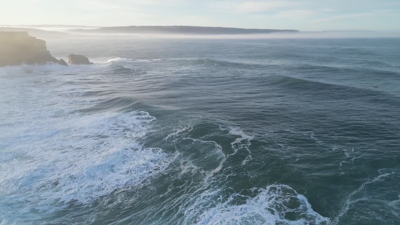 L'oceano vicino al Farol da Nazaré, Portogallo, con onde calme e scogliere, vista aerea.