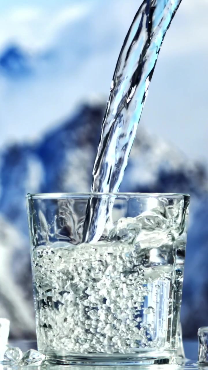 Acqua limpida che si versa in un bicchiere con ghiaccio su uno sfondo montano