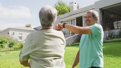 video de una feliz pareja de ancianos biraciales tomados de la mano y bailando en el jardín