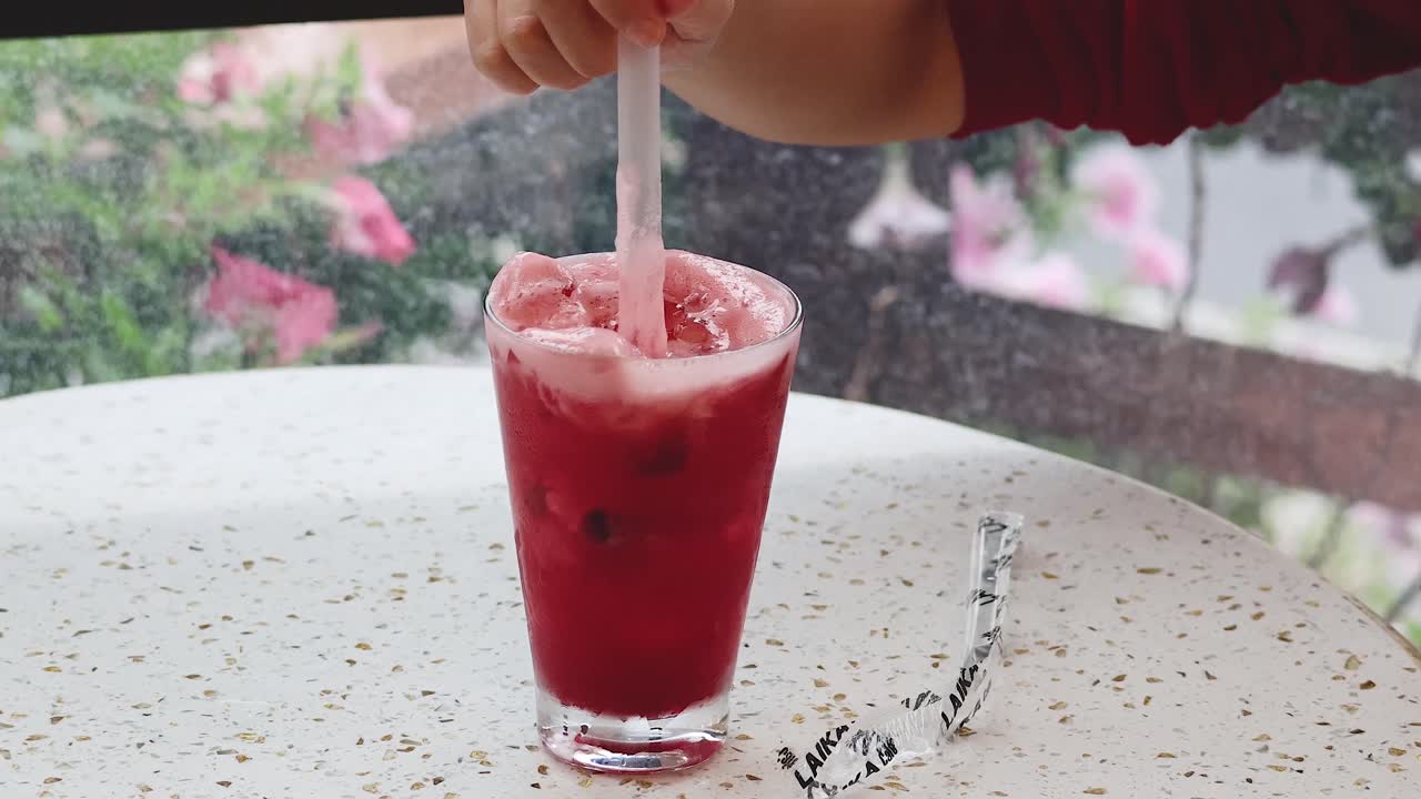 Mano che mescola una bevanda rossa con una cannuccia