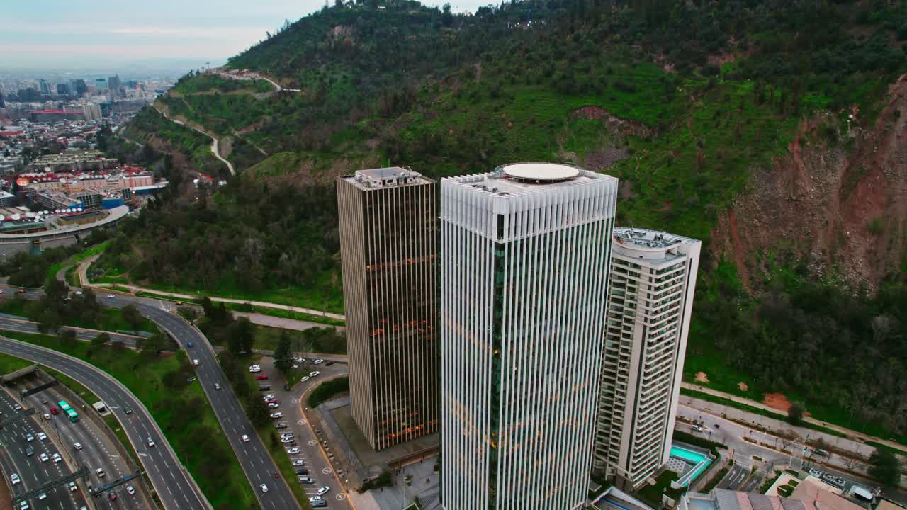 Vista aérea em tilt-down das Torres Santa Maria e do Parque Met em Santiago do Chile, com a autoestrada em baixo tráfego.