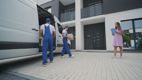 two young workers of removal company unload boxes from minibus into customer's home