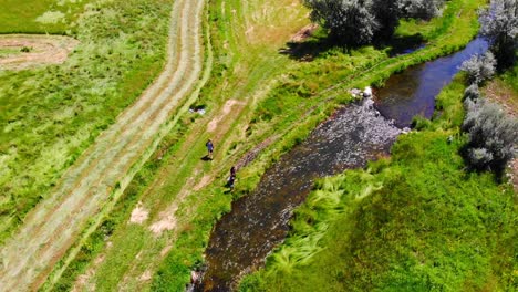 two people fishing on flowing river creek in lush green colorado countryside