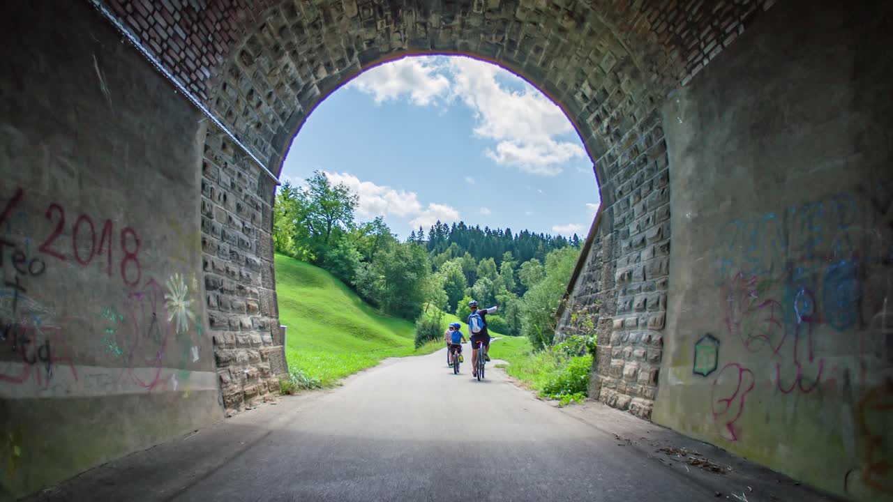 Active family ride bicycles through tunnel path in Slovenia, rear slomo