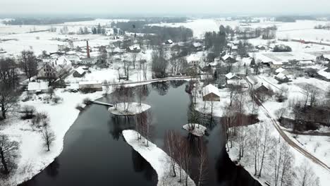 scenic smooth bird's-eye view over calm village by frosted lake at winter