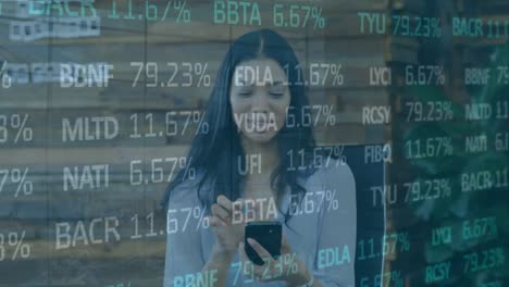 Animation-of-trading-board-over-happy-biracial-woman-talking-on-smartphone-in-office
