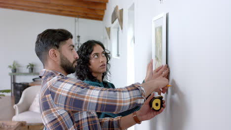 una feliz pareja biracial tomando medidas en la pared en casa, en cámara lenta