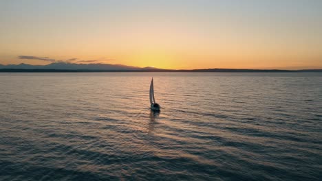 aerial orbiting shot of cruising sailing boat on the ocean enjoying golden sunset on the horizon