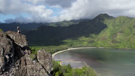 excursionista de pie en la cima del acantilado del sendero del león agachado con el parque de la playa de la bahía de kahana en verano en oahu, hawaii