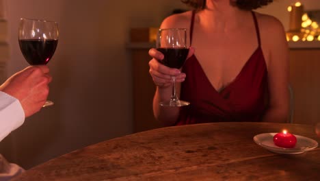 romántica mesa de cena con una pareja brindando con vasos de vino rojo