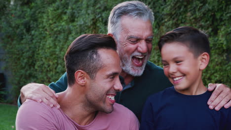 Porträt-Einer-Männlichen-Hispanischen-Mehrgenerationenfamilie-Im-Garten,-Die-In-Die-Kamera-Lächelt