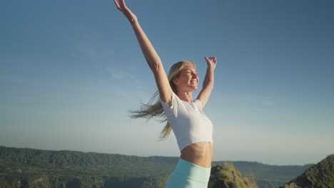 excursionista femenina que llega a la cima levantando los brazos en el aire expresión de la cara feliz y sentido de libertad