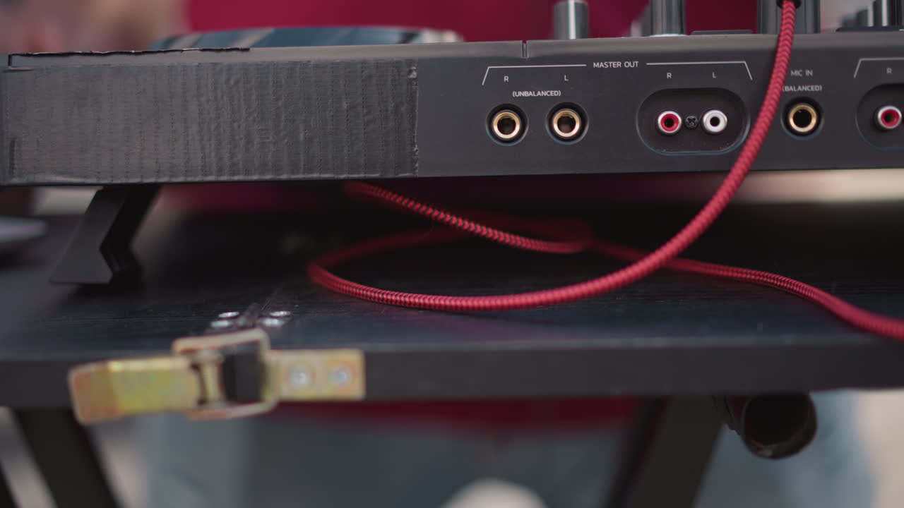 closeup hand connecting red cable mixer, fingers guiding braided cord into goldplated jack on compact controller, metal buckle and case edge visible, shallow depth of field, ambient club lighting