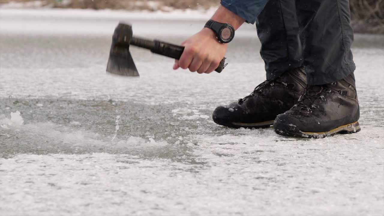 Fisherman breaking ice with an axe on a frozen lake in winter