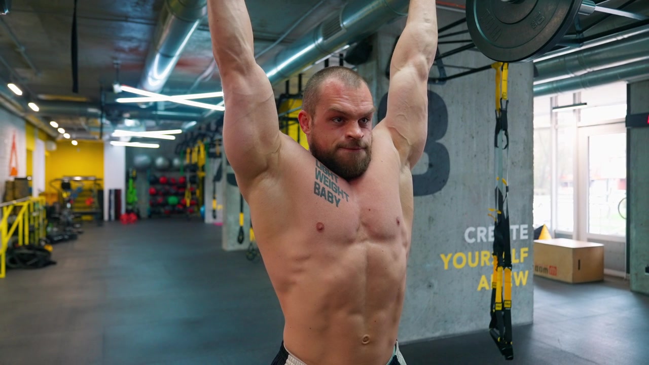 Uomo muscoloso che esegue una distensione sopra la testa con bilanciere in una palestra moderna