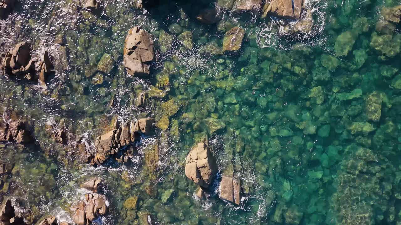 Low drone footage skimming the top of rocks as it passes over crystal clear water with views to the seabed wonderful rock formations and calm sea on sunny day