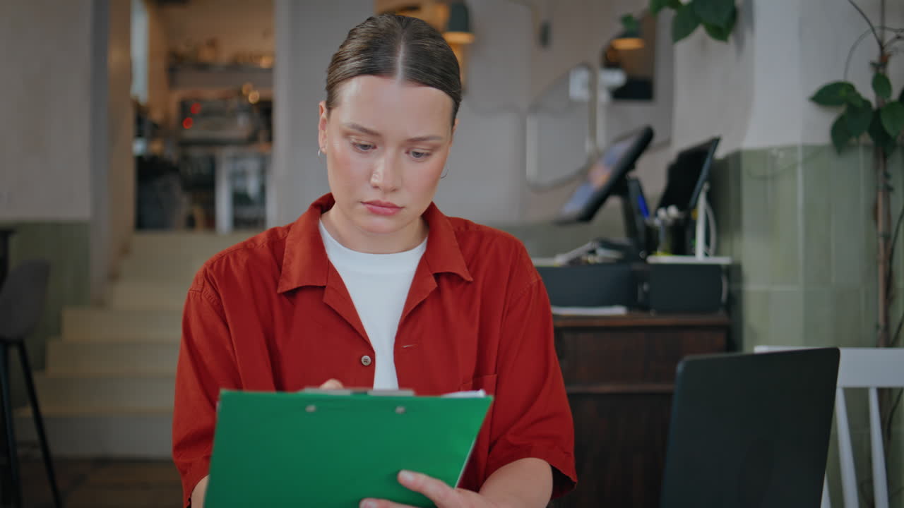 Thoughtful lady reading clipboard in cafeteria closeup. Serious restaurant owner