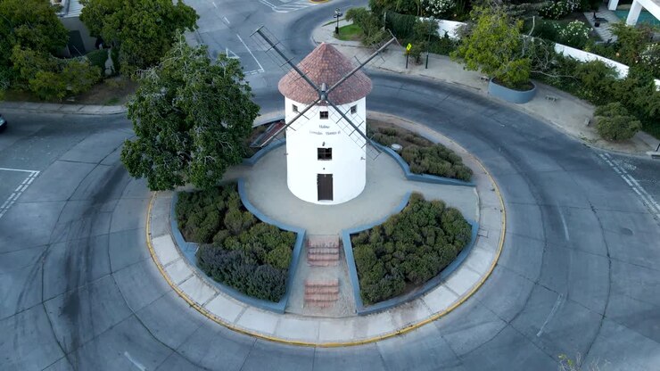 Afastamento aéreo da torre de moinho de vento Leonidas Montes em rotatória com veículos circulando, rodeada por árvores, Lo Barnechea, Santiago, Chile