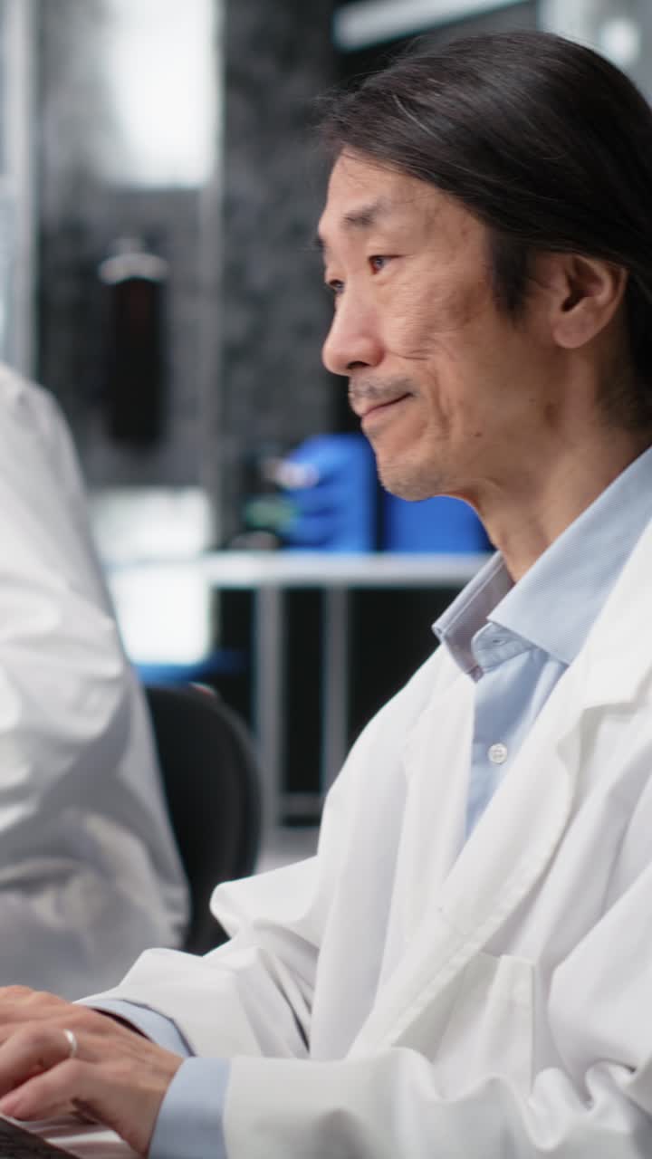 Vertical video Smiling Asian laboratory researcher using computer to process DNA patient data
