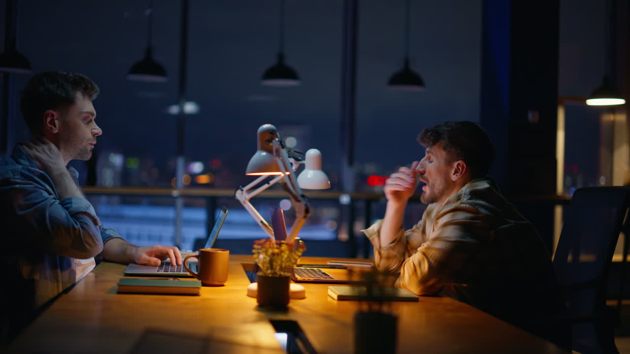 Tired freelancers working late at office room closeup. Brunette man stretching