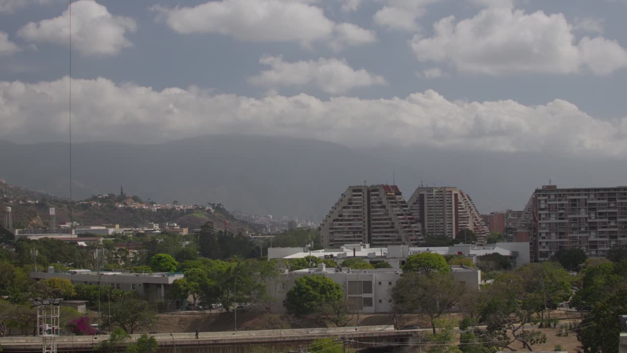 Vista panoramica degli edifici di Montalban a Caracas, Venezuela, con la maestosa montagna Avila sotto un cielo nuvoloso e tenue. Illuminazione calda e cinematografica che esalta l'architettura urbana e la natura.
