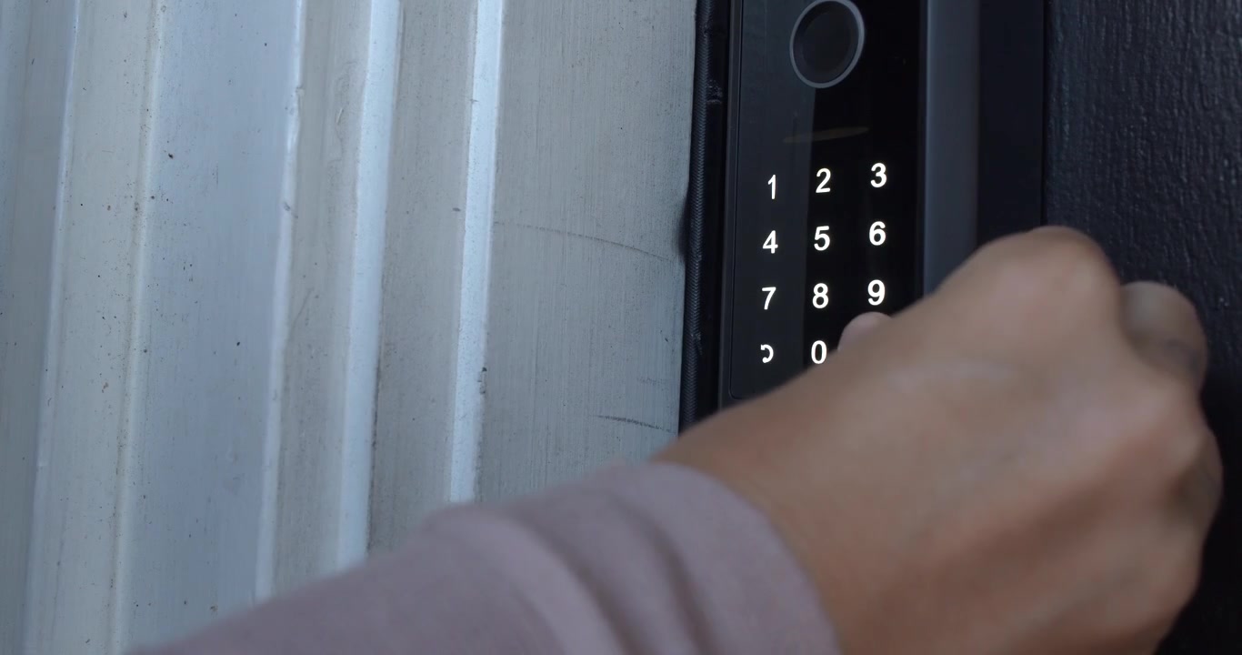 Close-up of a person touching a lock icon on an illuminated smart door lock keypad at a residential front door.