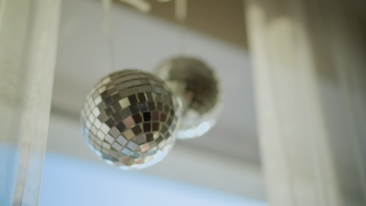 Mano de niño alcanzando bolas de discoteca brillantes colgadas en el interior cerca de la ventana; la luz del sol se refleja en las superficies espejadas creando un efecto de luz brillante, curiosidad juguetona y ambiente festivo