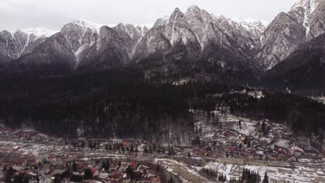 aerial shot flying over green pine trees in a mountain range covered with snow