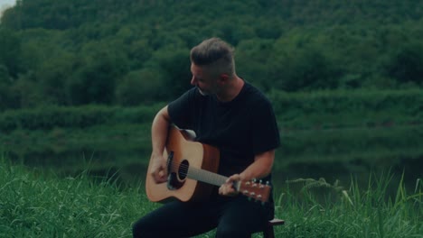 man playing acoustic guitar by a river in a forest