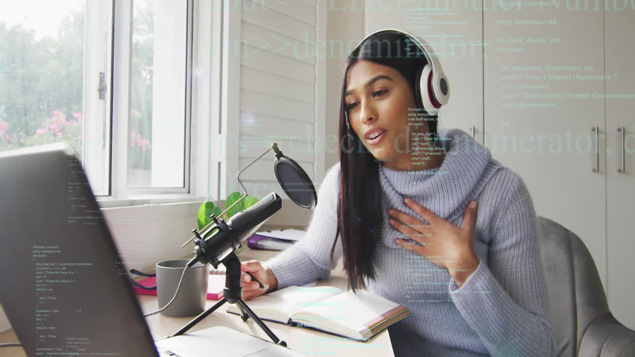 Woman leaning toward laptop and mic, reading notes and speaking while recording podcast at desk