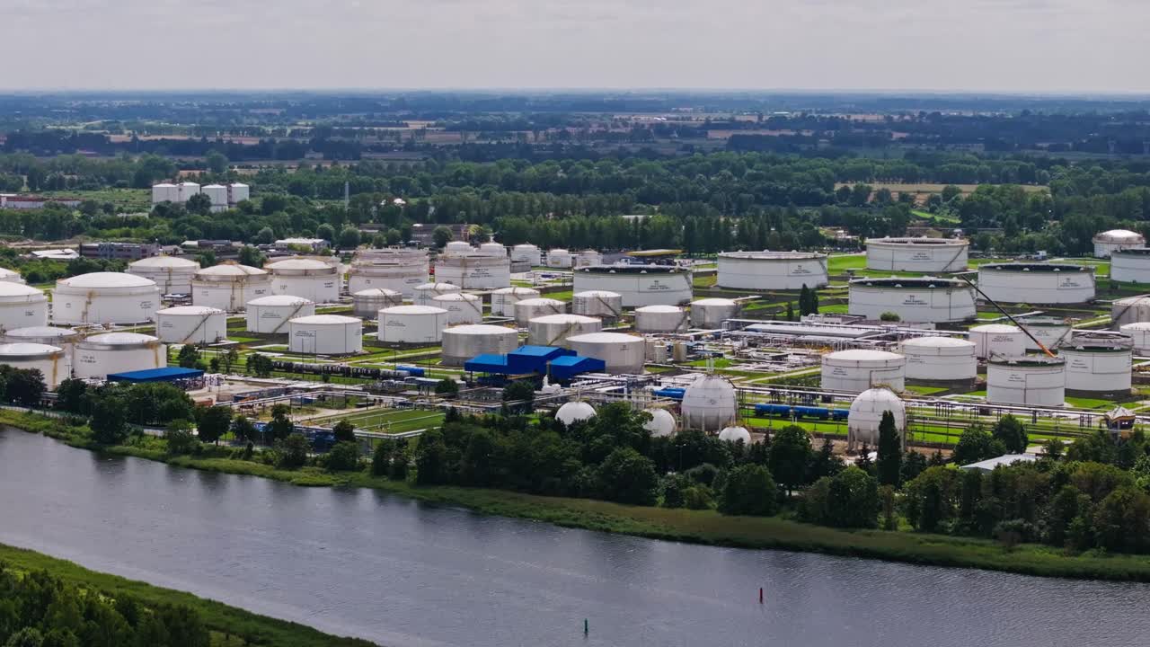 Drone cattura un'ampia vista della raffineria, mostrando serbatoi di carburante e condutture lungo il fiume.