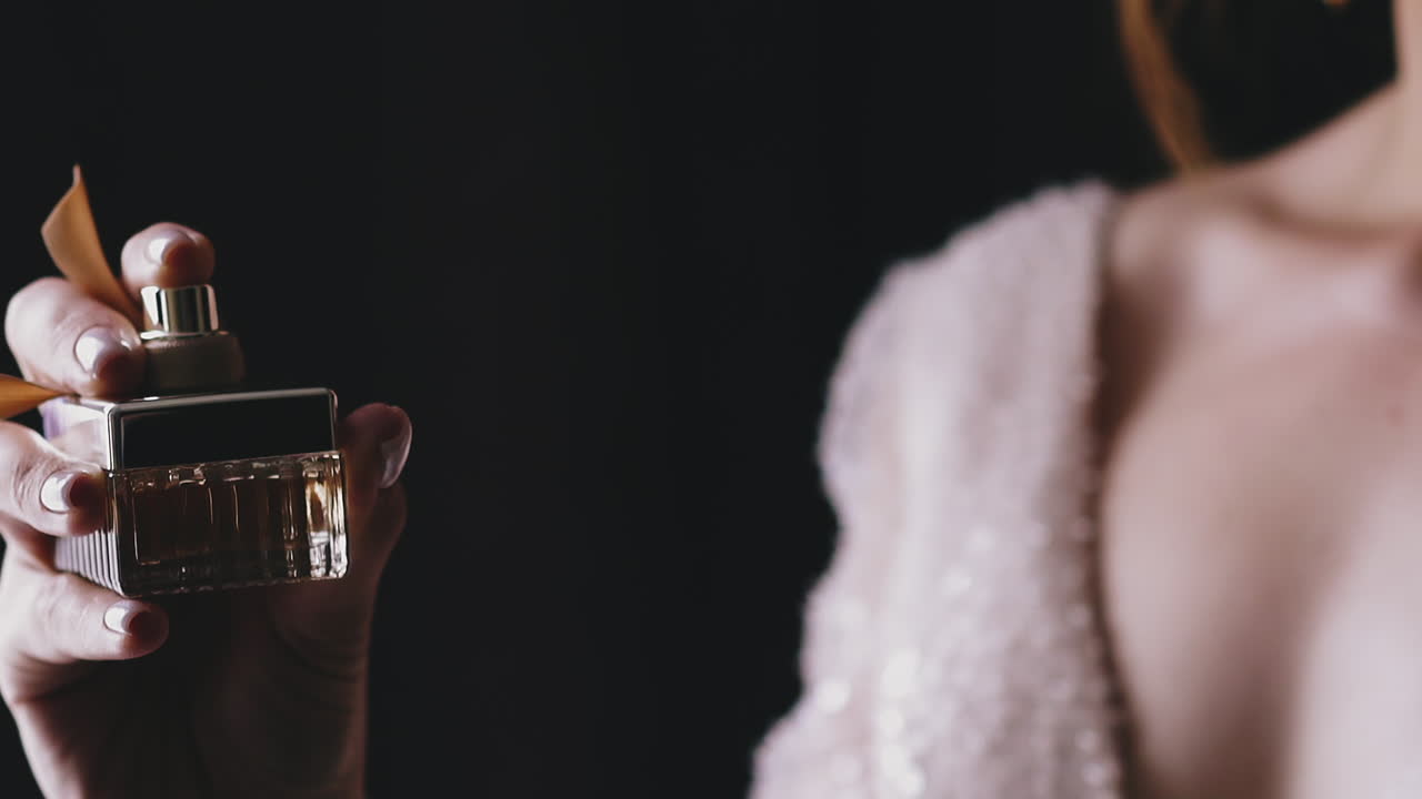 dama con vestido brillante rocía fragancia sobre fondo negro