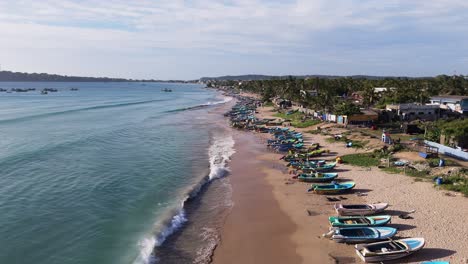 green blue wave formations lapping the white sandy shoreline with fishermen’s boars ontrincomalee beach, sri lanka. aerial drone fly over.