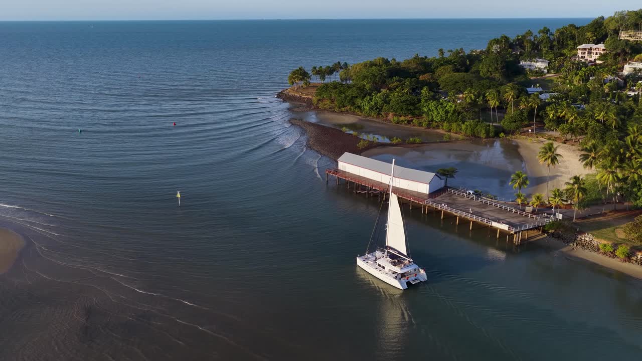 Drone footage captures a catamaran sailing near a tropical jetty surrounded by lush greenery and calm waters