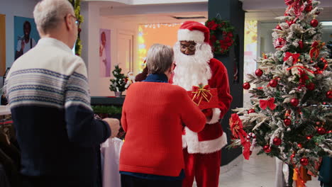 Dolly-in-shot-of-man-wearing-Santa-Claus-suit-holding-raffle-contest-in-Christmas-ornate-shopping-mall-clothing-store-during-winter-holiday-season,-looking-for-clients-to-participate