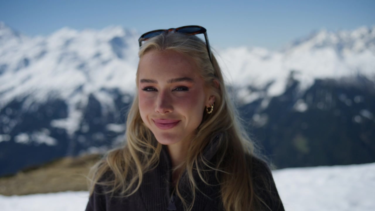 Ritratto in primo piano di una giovane donna che si gode il sole nelle Alpi svizzere. Cieli di un blu intenso e un'espressione rilassata creano una scena di viaggio invernale di lusso e di stile di vita all'aperto.