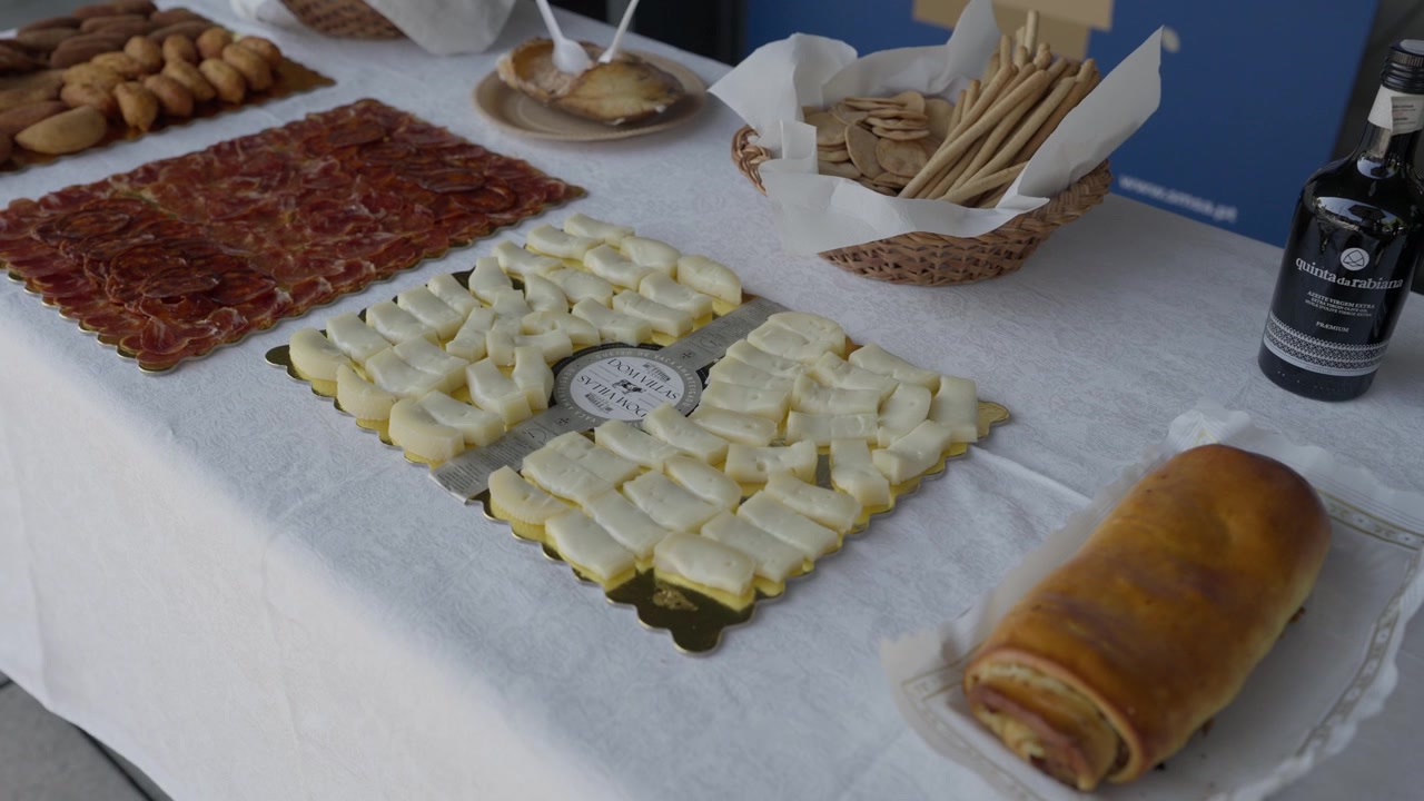 Skiveskåret spegeskinke og osteanretninger med brødstænger og folar på et hvidt buffetbord.