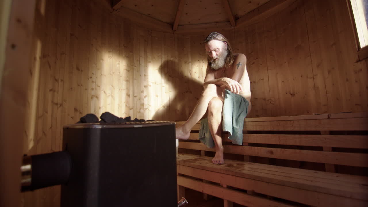 Ungroomed older man sit relaxed with crossed legs meditating inside wooden sauna