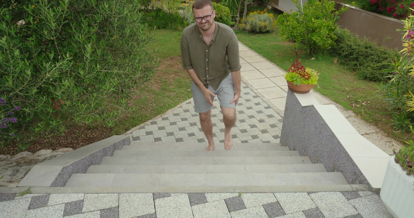 Slow motion scene of a man having difficulty walking down outdoor stairs, showing physical struggle and imbalance in a natural environment. Focus on effort, movement, and safety awareness.