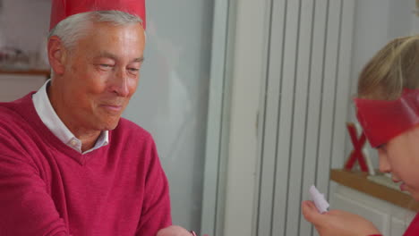 grandfather with granddaughter playing with christmas cracker gifts whilst eating meal together
