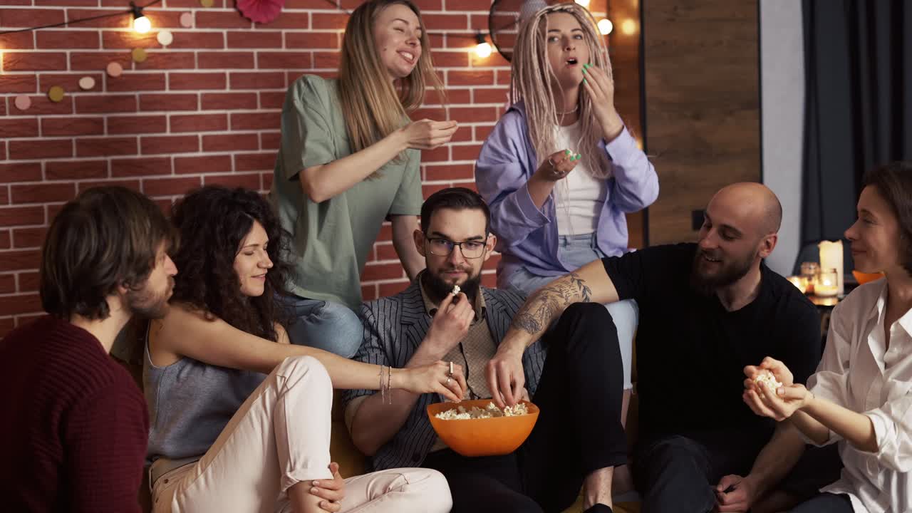 Amici che prendono popcorn da una ciotola mentre sono seduti su un divano a casa.