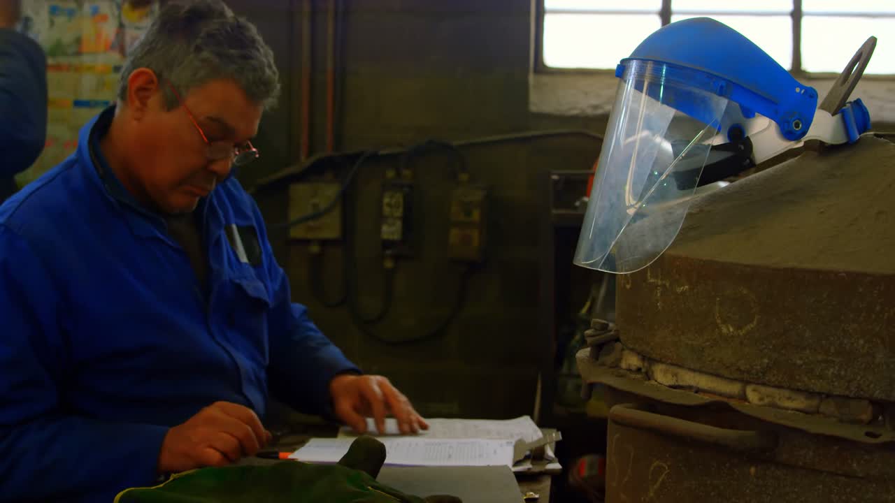 Operaio che scrive su un blocco appunti in un'officina di fonderia 4k