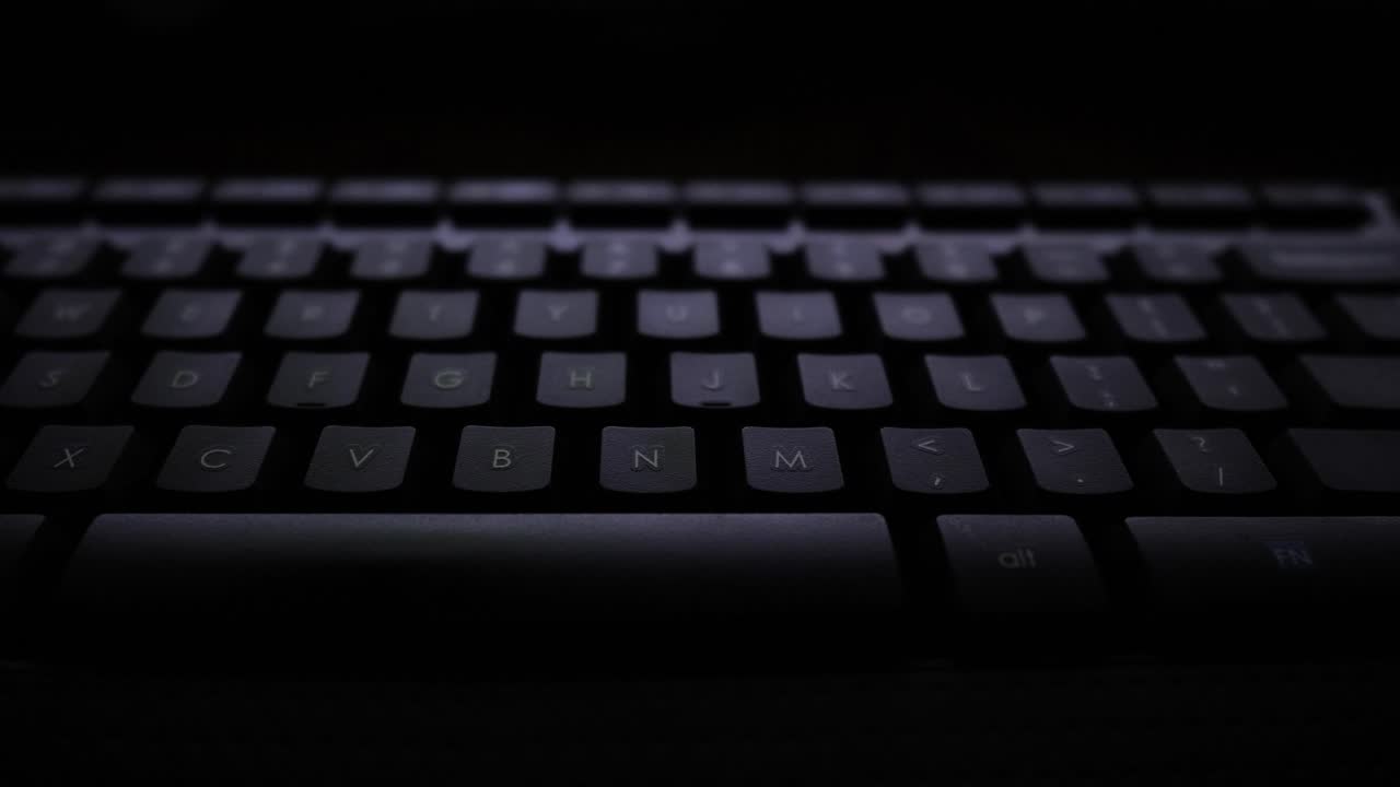 Panning shot of a keyboard lit by a computer screen.