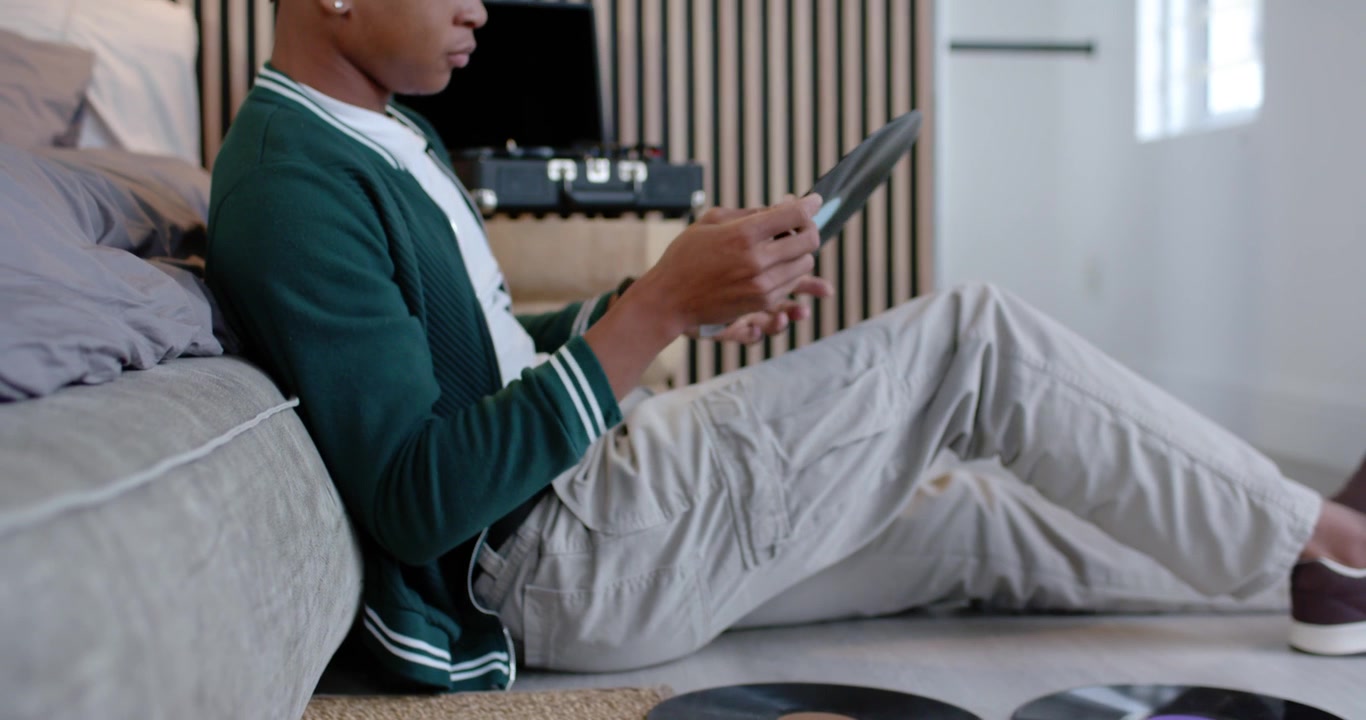 African American man reaching for records on rug, inspecting labels before playing on turntable